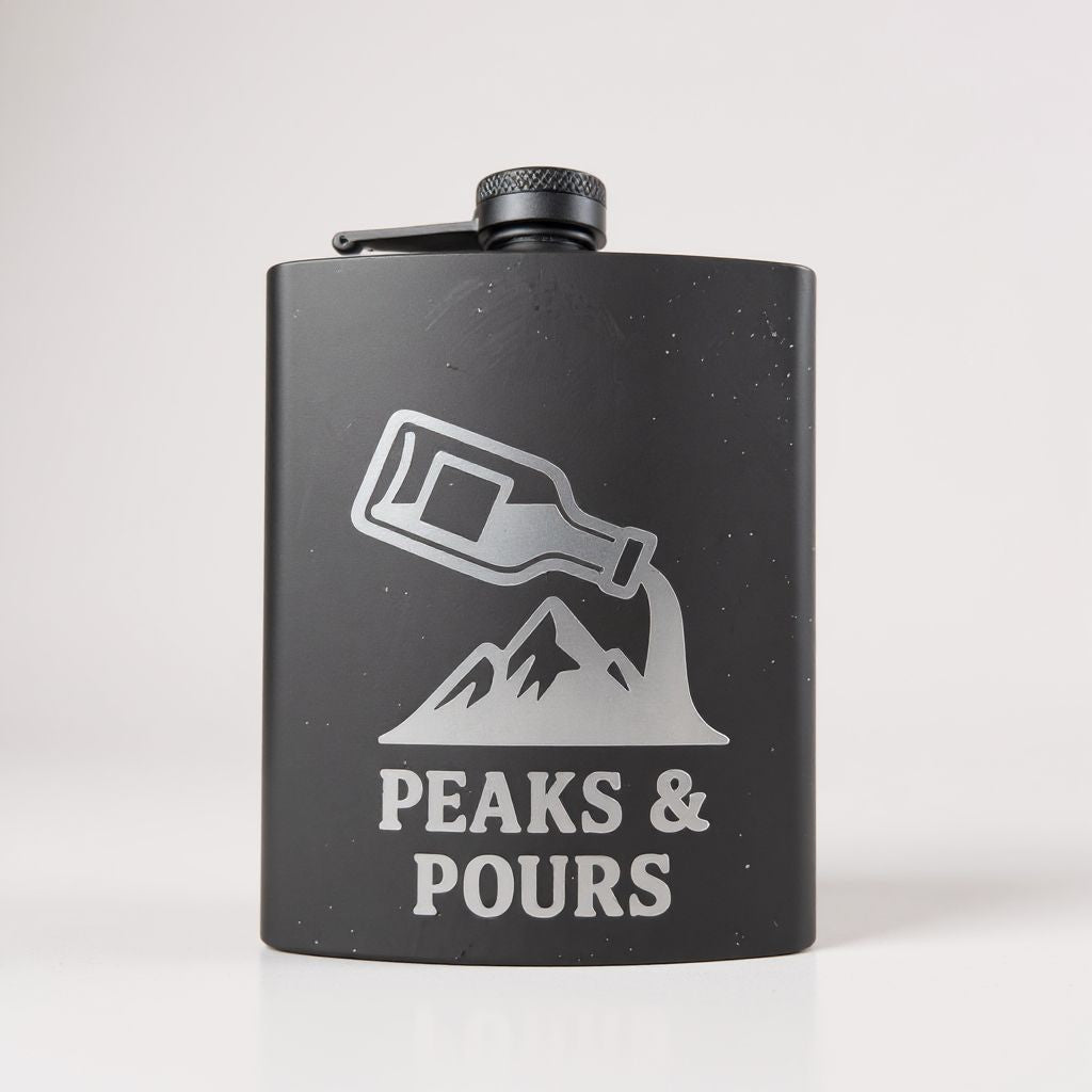 A matte black flask with a silver graphic of a bottle pouring into a mountain shape, with the text 'PEAKS & POURS' below, on a light gray background.