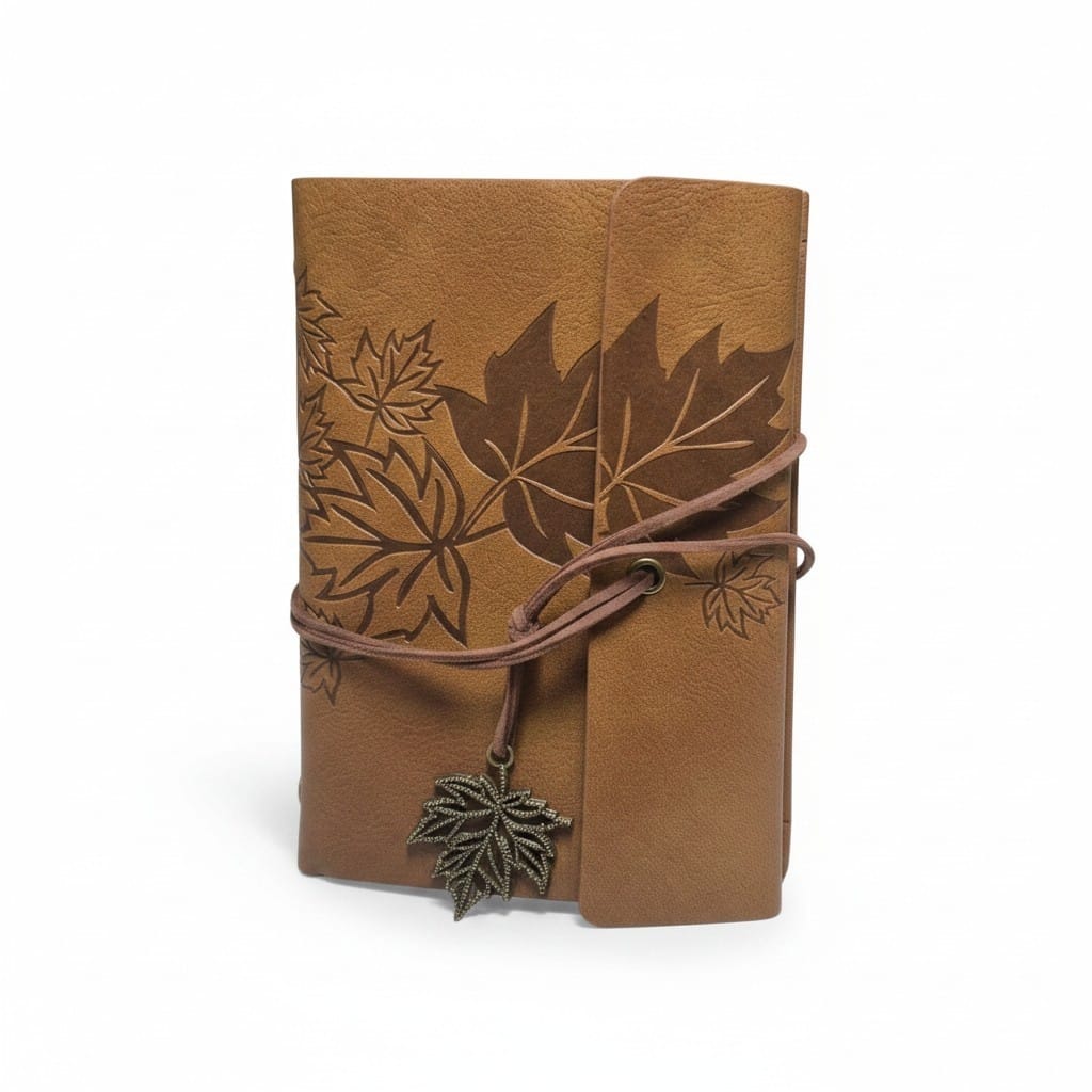 A brown leather journal with embossed maple leaf designs, wrapped with a matching leather cord and a small metal leaf charm, shown on a white background.