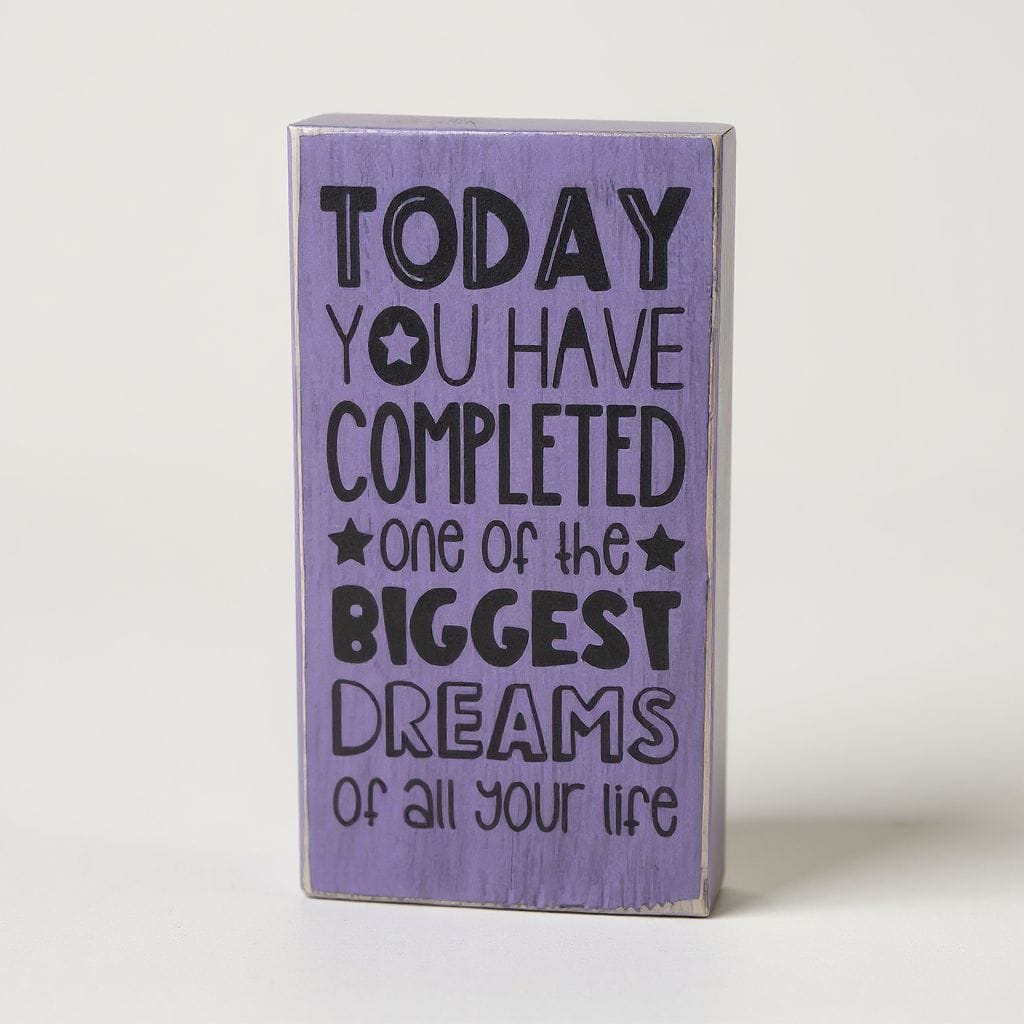 A rectangular lavender wooden block sign with black text that reads, 'TODAY YOU HAVE COMPLETED one of the BIGGEST DREAMS of all your life' on a light gray background.