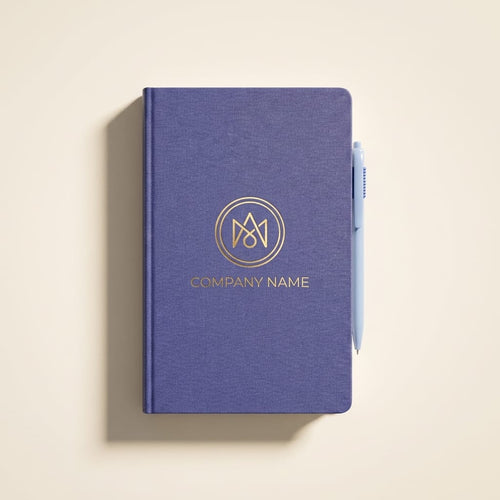 Custom navy blue hardcover journal with gold foil circular monogram logo and company name, flat lay on a clean cream background with a blue pen