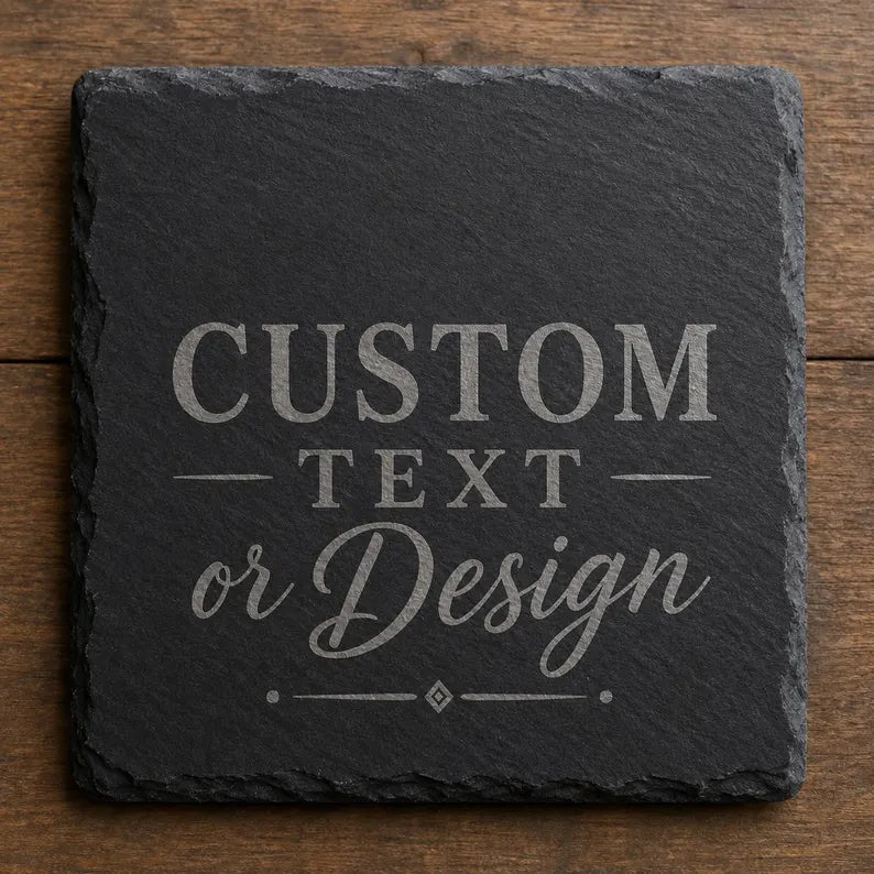 A square dark gray slate coaster with rough natural edges, featuring customizable light gray text or design placeholder text on the surface, displayed on a rustic brown wooden surface.