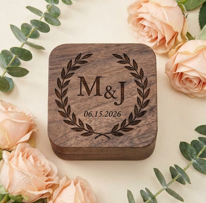 A square wooden keepsake box with rounded corners, engraved with a laurel wreath and the personalized text 'M&J 06.15.